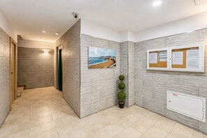 A hallway with a beach view painting, a bulletin board with notices, and a potted plant. - GuestReady - Salvador Cuyas Beach Walk (Las Palmas de Gran Canaria)