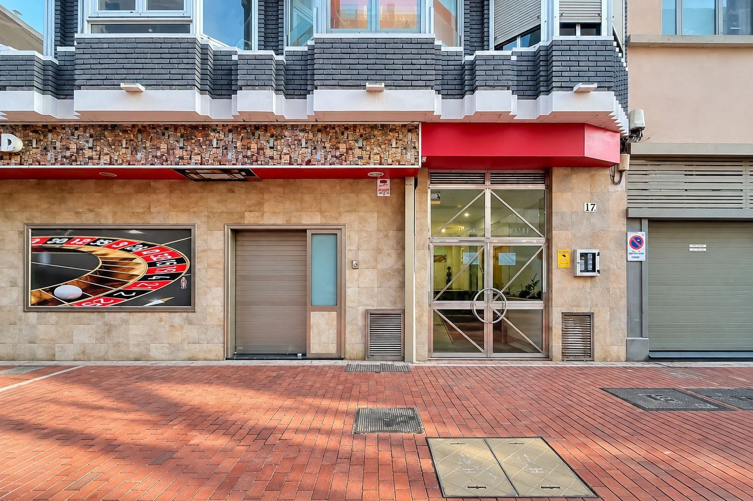 A building with a roulette wheel mural, a closed garage door, and a no parking sign.