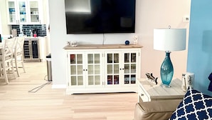 Una sala de estar con televisor de pantalla plana, un sofá, una lámpara y un aparador con puertas de vidrio.