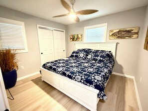 A bedroom with a bed, a ceiling fan, a window with blinds, and a wall-mounted artwork.