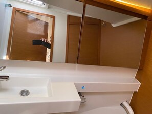 A bathroom with a white sink, a mirror, and a wooden door. - Sun-Kissed Sailing Adventure in Islas Baleares, Mallorca (Palma)