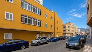 Katu, jonka varrella on parkkeerattuja autoja ja jonka toisella puolella on rivissä keltaisia rakennuksia, joissa on useita ikkunoita ja ikkunaluukut.