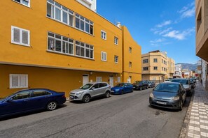 Eine Straße mit geparkten Autos und gelben Gebäuden mit zahlreichen Fenstern und Fensterläden.