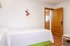 A room with a single bed, a green bedside table, a wooden door, and a wall-mounted light fixture.