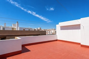 Une terrasse sur le toit avec un sol rouge, des murs blancs et un ciel d’un bleu éclatant.