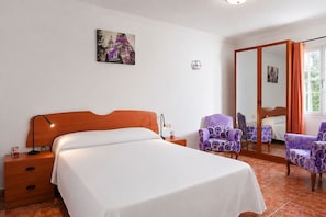 Ein Schlafzimmer mit einem Bett, einem Nachttisch, einem Sessel, einem Spiegel und einem Bild an der Wand.