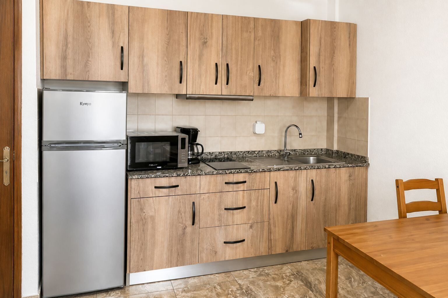 Una cocina con armarios de madera, un refrigerador de acero inoxidable, un microondas, una cafetera y un lavamanos.
