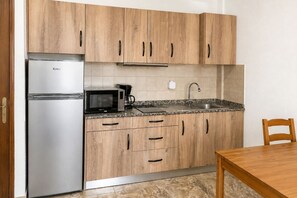 Eine Küche mit Holzschränken, einem Edelstahlkühlschrank, einer Mikrowelle, einer Kaffeemaschine und einem Spülbecken.