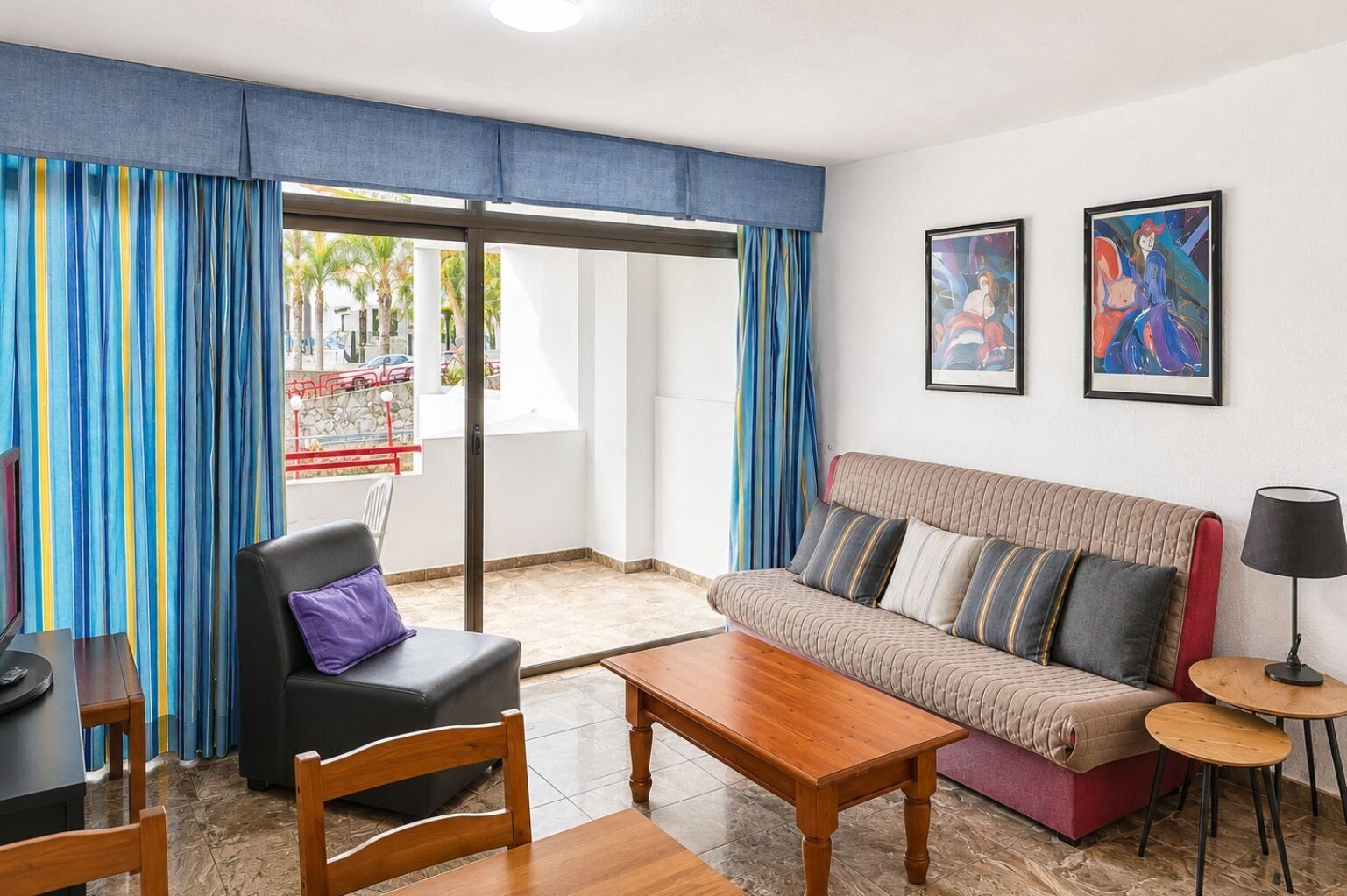 A living room with a sofa, a chair, a table, and a lamp. There are two framed pictures on the wall.