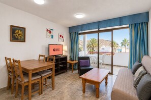 Ein möbliertes Wohnzimmer mit Esstisch, Stühlen, einer Couch, einem Fernseher und einem Balkon mit Aussicht.
