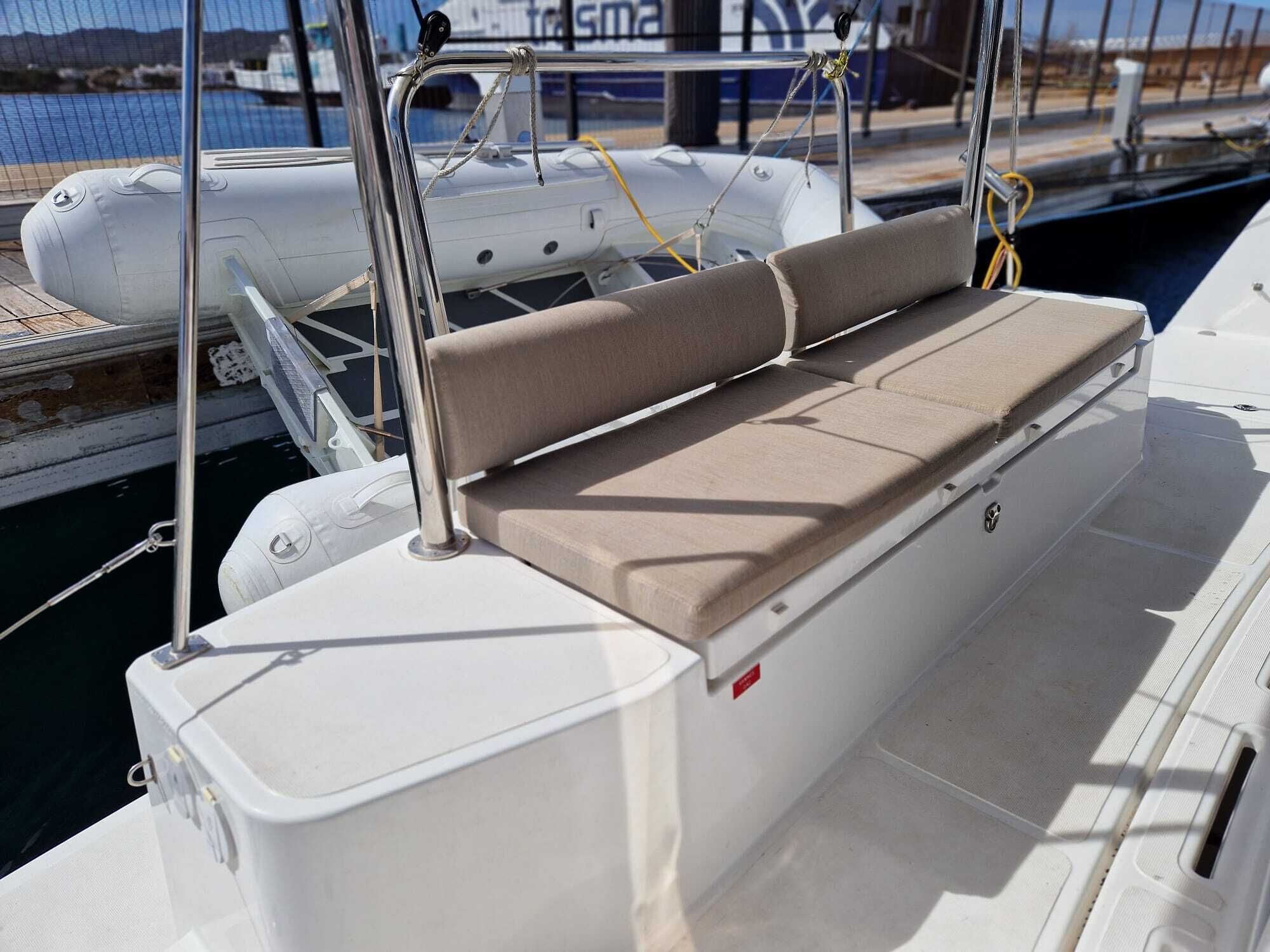 Le pont d’un bateau, doté d’une zone de sièges rembourrés, avec une coque blanche et une marina en arrière-plan.