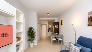 Una sala moderna con sofá, televisor, zona de comedor con sillas y cocina al fondo.