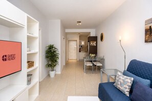 Ein modernes Wohnzimmer mit einer Couch, einem Fernseher, einem Essbereich mit Stühlen und einer Küche im Hintergrund.