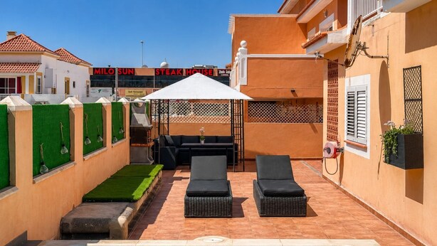 Un área de piscina con sillones de descanso, una parrilla y una zona de estar cubierta.