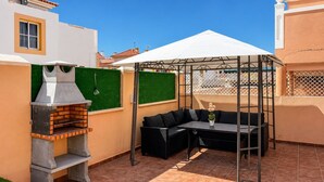Un patio con una parrilla, mobiliario exterior y un área techada.
