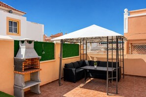 Eine Terrasse mit Grill, Gartenmöbeln und einem überdachten Bereich.