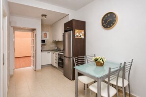 Eine moderne Küche mit einem Edelstahl-Kühlschrank, einem Esstisch mit Stühlen und einer Wanduhr.
