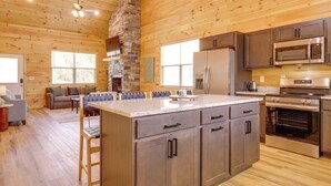 A wooden cabin interior with a kitchen featuring granite countertops, stainless steel appliances, and a stone fireplace. - Dolly's Cabin: Walk to Dollywood Private Spa View (Pigeon Forge)