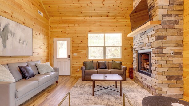A log cabin interior with a stone fireplace, a sofa, a coffee table, and a door. - Dolly's Cabin: Walk to Dollywood Private Spa View (Pigeon Forge)
