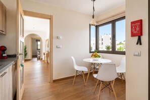 Een moderne keuken met houten kastjes, een eethoek met witte stoelen, en een raam met uitzicht op gebouwen.