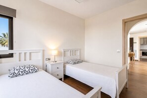 Een slaapkamer met twee bedden, een nachtkastje met een lamp en uitzicht op de keuken door een geopende deur.