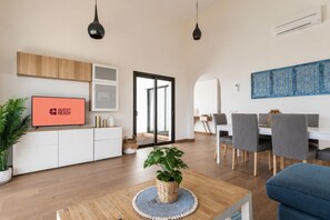 A modern living room with a TV, a dining area with chairs, a large window, and a plant on a wooden table. - GuestReady - Luxury Villa with Private Pool (Antigua)