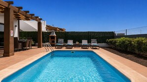 Ein rechteckiger Pool mit einer Holzpergola an einer Seite, Liegestühlen und einem Grill.