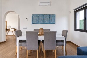 A dining area with a white table, grey upholstered chairs, and a decorative blue panel above. - GuestReady - Luxury Villa with Private Pool (Antigua)