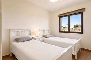 A bedroom with two beds, a nightstand, a lamp, and a window with a view. - GuestReady - Luxury Villa with Private Pool (Antigua)