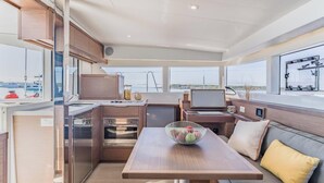 A compact kitchen with modern appliances, a dining area with a table and seating, and a large window providing a view of the sea. - Sun-kissed Sailing Adventure in Split-Dalmatia, Croatia (Trogir)
