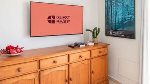A wooden cabinet with a flat-screen TV displaying 'GUEST READY' and a poster of a forest scene. - GuestReady - Arenas Charming Pool (Caleta de Fuste)