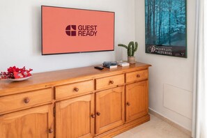 Ein Holzkabinent mit einem Flachbildfernseher, der 'GUEST READY' anzeigt, und einem Poster mit einer Waldszene.