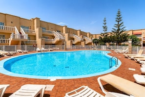 A swimming pool with sun loungers and a building with balconies. - GuestReady - Arenas Charming Pool (Caleta de Fuste)