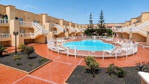 A pool area with a circular pool, surrounded by a white fence, and multiple balconies with railings. - GuestReady - Arenas Charming Pool (Caleta de Fuste)