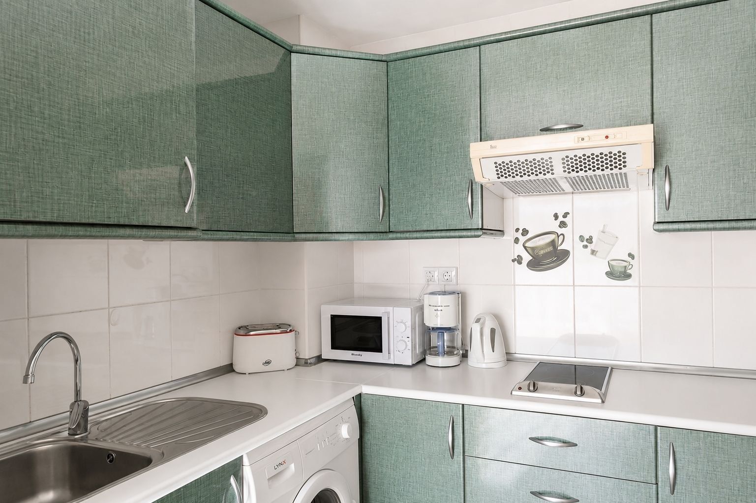 A kitchen with green cabinets, a sink, a toaster, a microwave, a coffee maker, and a washing machine.