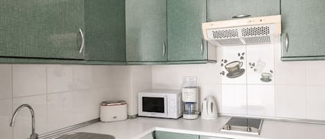Une cuisine avec des meubles de rangement verts, un évier, un grille-pain, un four à micro-ondes, une machine à café et un lave-linge.
