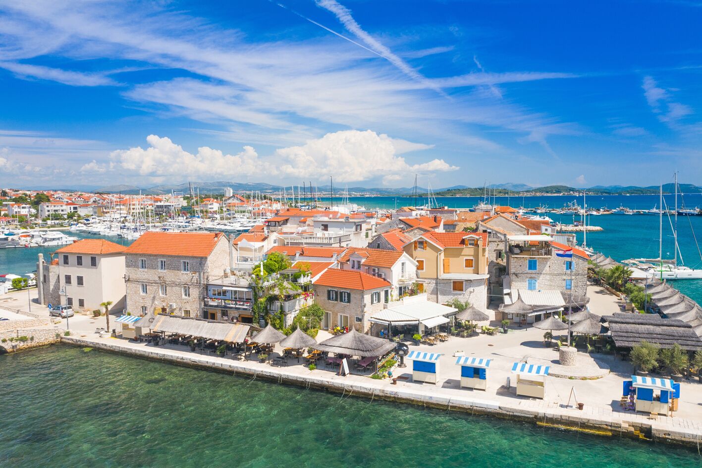 Un pueblo costero con edificios de piedra, un puerto deportivo y cielos azules despejados.