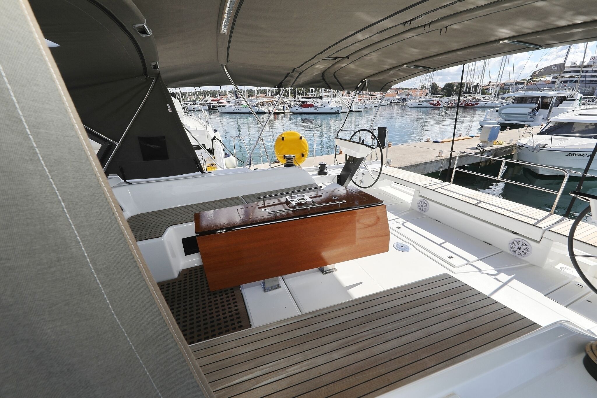 Coixinet d'una embarcació amb una consola de fusta, un bou de salvament groc i un port esportiu amb diverses embarcacions al fons.