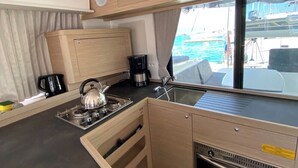 A compact kitchen with a stove, kettle, and coffee maker, a window with a view of the sea, and a small oven. - Sun-kissed Sailing Adventure in Split-Dalmatia, Croatia (Trogir)