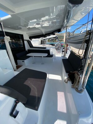 Convés de barco com áreas de estar, uma mesa e uma corda enrolada ao lado.