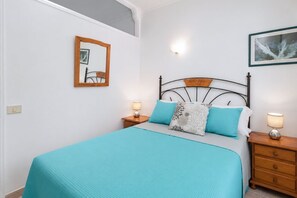 Ein ordentlich eingerichtetes Schlafzimmer mit einem Bett, zwei Nachttischen, einem Wandspiegel und einem gerahmten Bild.