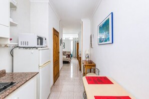 Ein schmaler Flur mit einer Küche an einer Seite, einem Essbereich mit Tisch und Stühlen und einem Sofa im Hintergrund.