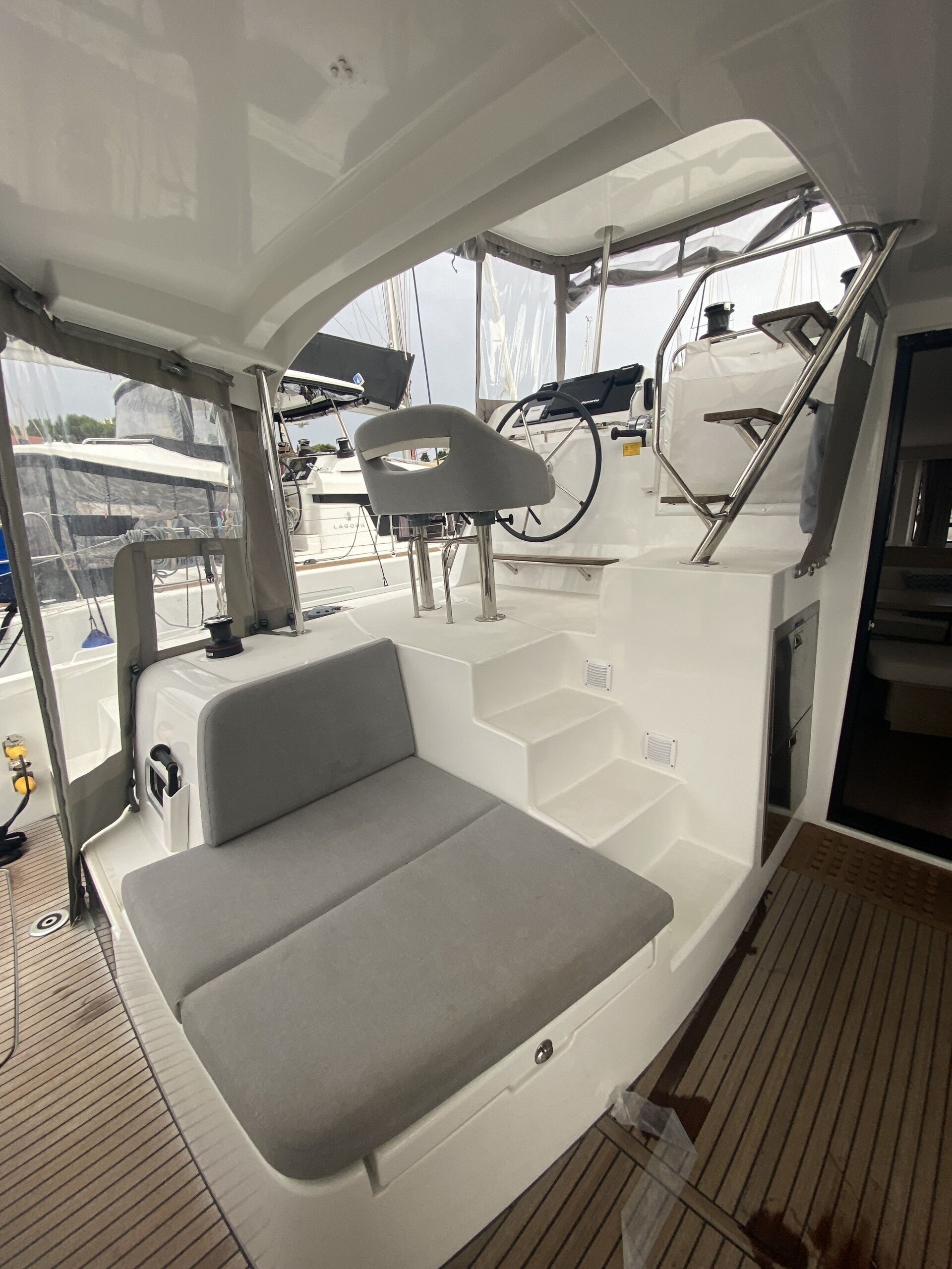 A boat deck with a cushioned seating area, a steering wheel, and a ladder.