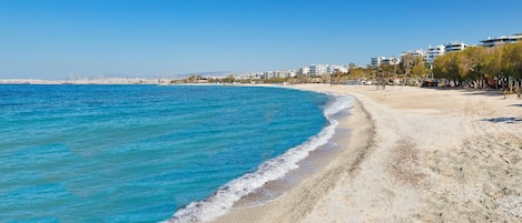 Une plage avec une eau d’un bleu limpide, un rivage sablonneux et des bâtiments en arrière-plan.