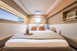 A narrow, well-lit bedroom with a bed, a small table with a cup, and a skylight above. - Sun-Kissed Sailing Adventure in Islas Sarónicas (Alimos)