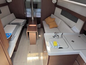 Ein kompakter, gut beleuchteter Innenraum mit Bett, Schlafsofa, kleinem Tisch und Küchenzeile.