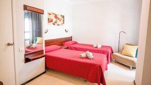 A hotel room with two single beds, a bedside table, a chair, a mirror, and a painting on the wall. - GuestReady - DiMar Sea View Premium (Las Palmas de Gran Canaria)