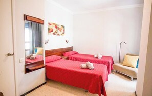 Ein Hotelzimmer mit zwei Einzelbetten, einem Nachttisch, einem Sessel, einem Spiegel und einem Bild an der Wand.