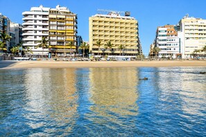 A beachfront hotel with multiple floors, a sandy beach in the foreground, and palm trees. - GuestReady - DiMar Sea View Premium (Las Palmas de Gran Canaria)