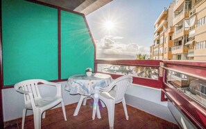 Ein Balkon mit Tisch und Stühlen, Blick auf das Meer, und ein Gebäude im Hintergrund.